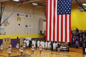 Puyallup High School cheerleaders and basketball team salute the flag as the Puyallup High School Pep Band plays the National Anthem.
