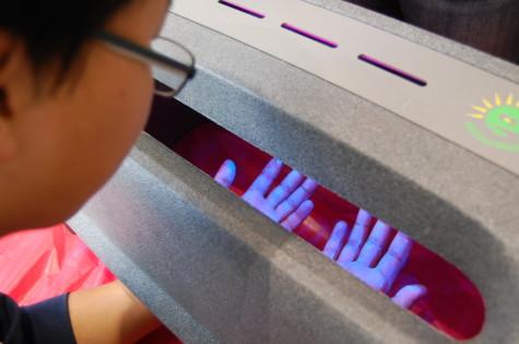 Junior Tae Kim examines his hands under a blacklight at the handwashing booth. HOSA is trying to make students aware of the importance behind throughly washing ones hands. 