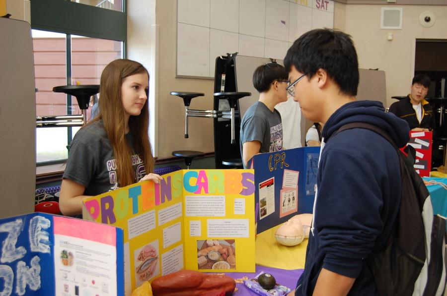 Sophomore and HOSA member Hannah Custer explains the difference between fats, carbohydrates and proteins to junior Tae Kim. The Health Occupation Students of America club held their annual spring health fair March 26.